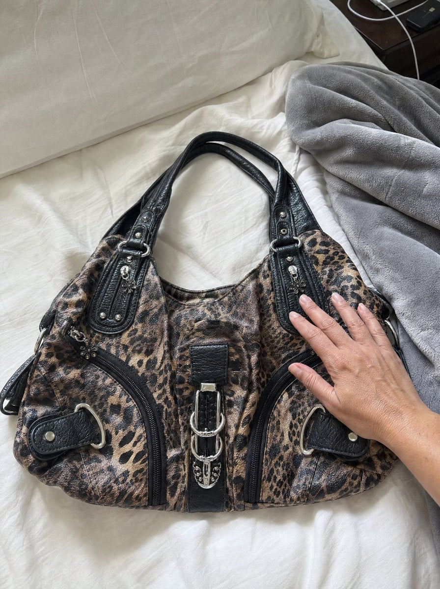 Leopard bag lying on a bed, hand resting on it